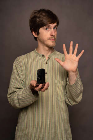 Young handsome tall slim white man with brown hair holding hand in the air holding black crystal in striped shirt on grey backgroundの写真素材