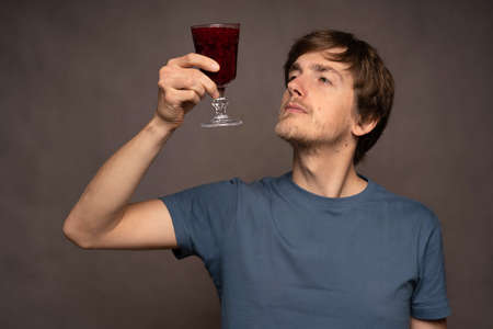 Young handsome tall slim white man with brown hair observing colour of smoothie in grey shirt on...