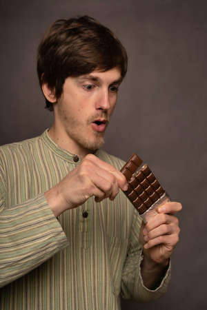 Young handsome tall slim white man with brown hair breaking off piece of chocolate looking excited...