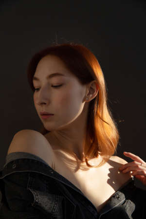 Young european woman with white skin isolated on black in black clothes with red hairの写真素材