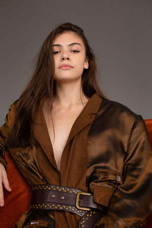 Portrait of young woman with long dark hair and brown eyes with dark grey wall behind
