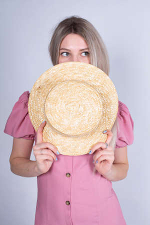 Woman with blonde hair and white skin isolated on grey in pink hiding behind a hatの写真素材