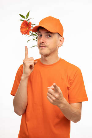 Young handsome tall slim white man with brown hair orange flower behind his ear pointing at it with orange shirt isolated on white backgroundの写真素材