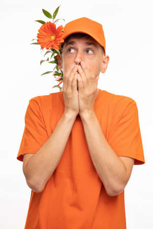 Young handsome tall slim white man with brown hair covering his mouth with orange flower behind ear...