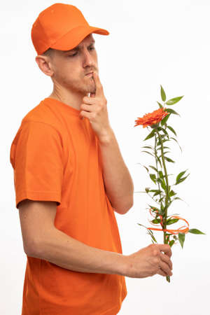 Young handsome tall slim white man with brown hair thinking watching orange flower with orange shirt and orange cap isolated on white backgroundの写真素材