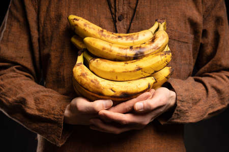White man holding bananas on his chest with brown shirt on black backgroundの写真素材