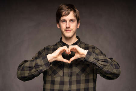 Young handsome tall slim white man with brown hair making heart with hands with flannel shirt on grey backgroundの写真素材