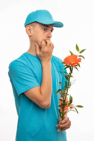 Young handsome tall slim white man with brown hair biting his nails holding orange flower with blue...