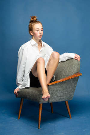 European girl with red hair and white skin isolated on blue sitting on chair