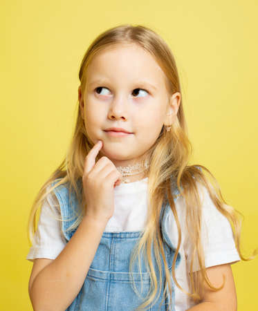 Thinking baby girl with blonde hair isolated on yellow