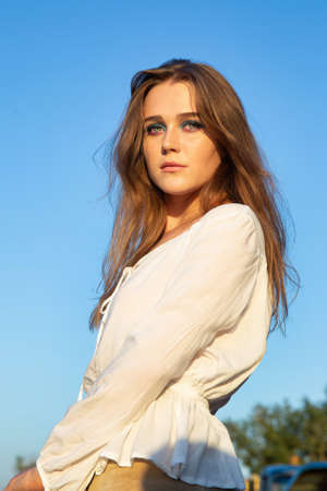 Serious young woman with white skin with sky behind in sunset light