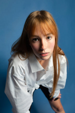 Closeup portrait of girl with red hair and white skin isolated on blue in shirtの写真素材