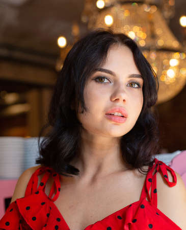 Portrait of young dark haired woman with white skin with lights behind with plump lips and...