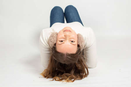 Young woman in warm white jumper with fur earmuffs isolated on white lying on the floorの写真素材