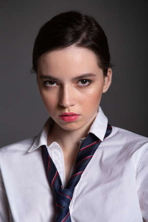 Portrait in business style of european young woman in white shirt wearing man tie isolated on black with plump lipsの写真素材