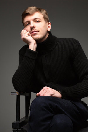 Boring young blond european man with short beard and mustache isolated on dark greyの写真素材