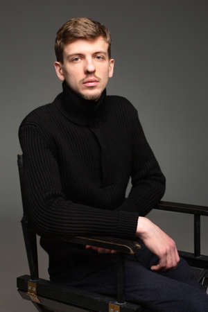 Portrait of young blond european man with short beard and mustache sitting isolated on dark greyの写真素材