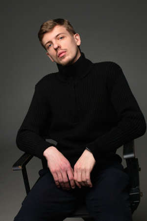 Young blond european man with short beard and mustache isolated on dark grey in total black outfitの写真素材
