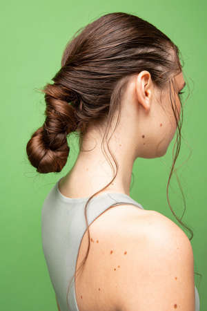 Turned back young woman with gathered dark hair isolated on greenの写真素材