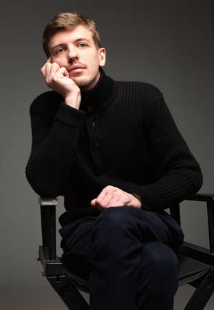 Boring young blond european man with short beard and mustache isolated on dark greyの写真素材