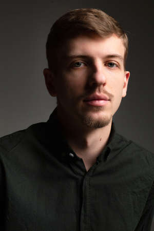 Portrait of young blond european man with short beard and mustache isolated on dark grey with shadow on his faceの写真素材