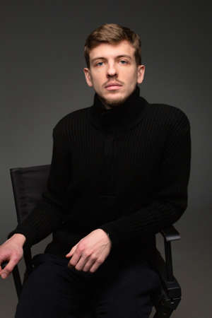 Young blond european man with short beard and mustache isolated on dark grey in total blackの写真素材