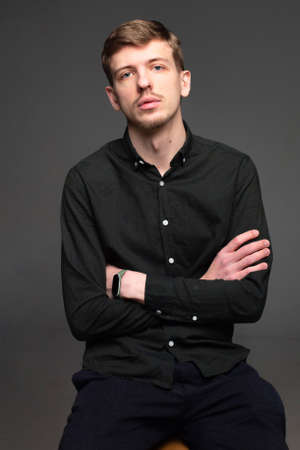 Young blond european man with short beard and mustache isolated on dark grey with folded armsの写真素材
