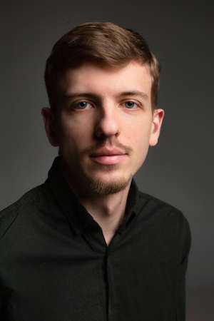 Portrait of young blond european man with short beard and mustache isolated on dark grey in black clothesの写真素材