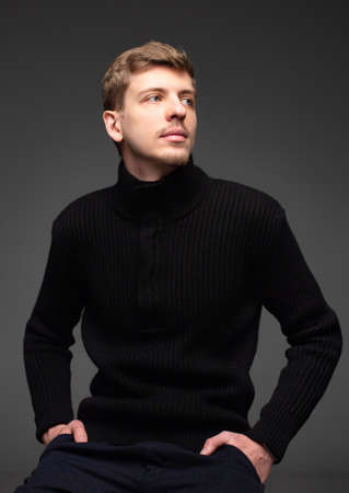 Young blond european man with short beard and mustache isolated on dark grey in total blackの写真素材
