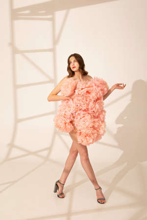 Walking young woman in dress made of coral pink flowers isolated on beige with ladder shadowの写真素材