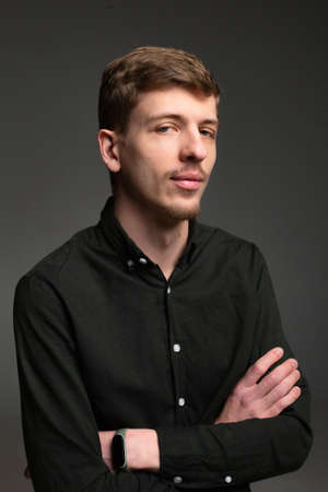 Smiling young blond european man with short beard and mustache isolated on dark grey with folded armsの写真素材