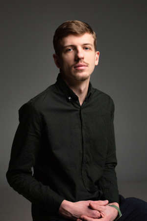 Young blond european man with short beard and mustache with clasped hands isolated on dark grey in black clothesの写真素材