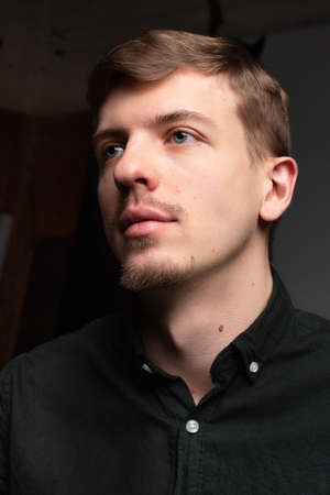 Portrait of young blond european man with short beard and mustache isolated on dark grey in black clothesの写真素材