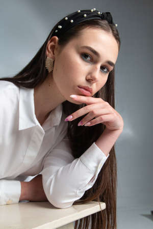 Portrait of young woman with dark hair in white long sleeve blouse isolated on greyの写真素材