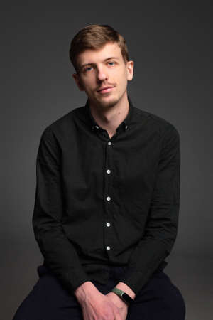 Young blond european man with short beard and mustache isolated on dark grey