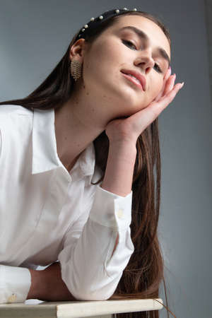 Portrait of smiling young woman with dark hair in white long sleeve blouse isolated on grey with hand near the faceの写真素材
