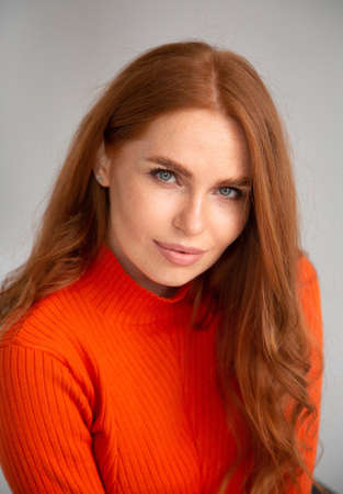 Portrait of woman with long red hair in orange jumper isolated on light grey
