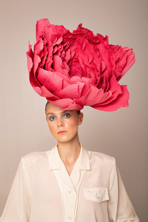 Portrait of young woman wearing pink peony hat with bright pink blush isolated on dark beigeの写真素材