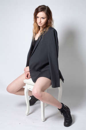 White young european woman sitting on the chair isolated on light grey in total blackの写真素材