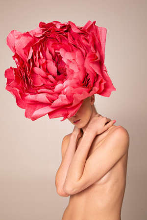 Naked young woman wearing pink peony hat isolated on dark beigeの写真素材
