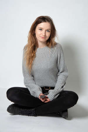 White young european woman with long curly hair in grey knitted jumper sitting isolated on greyの写真素材