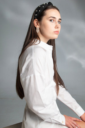 Young woman with dark hair in white long sleeve blouse isolated on greyの写真素材