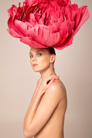 Naked young woman wearing pink peony hat isolated on dark beigeの写真素材