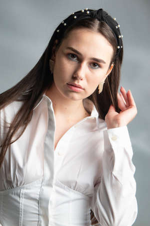 Portrait of young woman with dark hair in white long sleeve blouse isolated on greyの写真素材