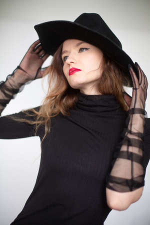 White young european woman in total black isolated on grey holding her hat by fingersの写真素材