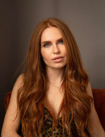 Portrait of woman with long red hair in animal print dress with gray eyes in dark roomの写真素材