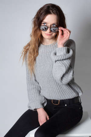 White young european woman with long curly hair in grey knitted jumper isolated on grey holding her glassesの写真素材