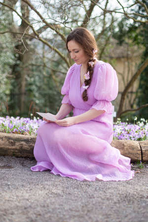 European woman in lilac dress with brown hair in park and reading a letterの写真素材
