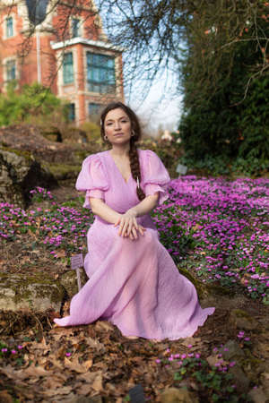 European woman in lilac dress with dark hair in park with house behindの写真素材