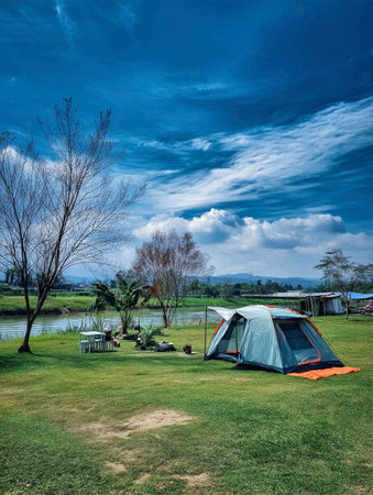 Camping under a clear blue sky with a tent by the river surrounded by nature outdoor adventure conceptの素材